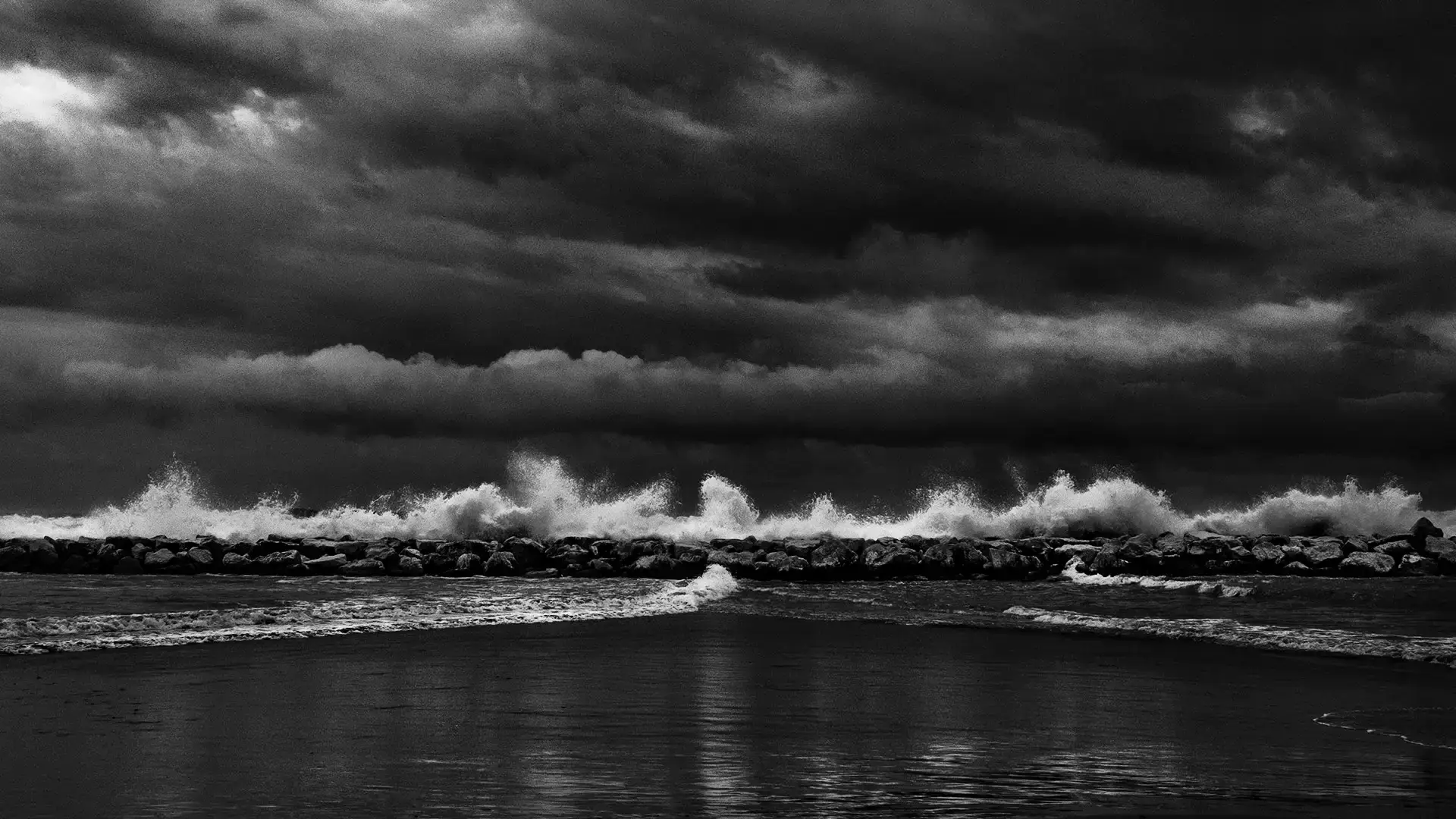 Onde che si infrangono sulla scogliera sotto un cielo carico di nuvole, fotografia in bianco e nero di Antonio Manno